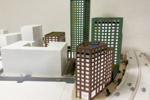 Architectural sales model 1:150 scale. Five highrise buildings painted green and brown brick. White offiste buildings. The architectural model is animated with trees.