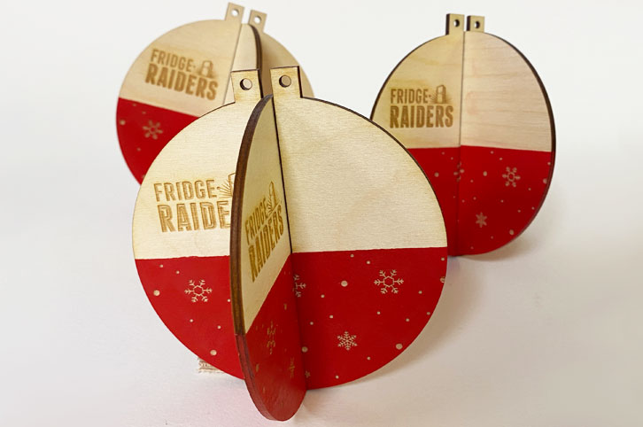 Laser cut slot together Christmas baubles made from laser cut plywood. They are painted red and laser engraved with Fridge Raiders logo. .