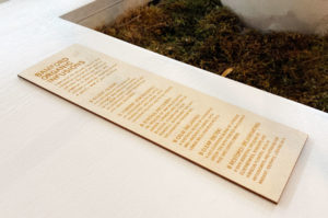 Engraved plywood menu sitting on a table next to natural moss feature.