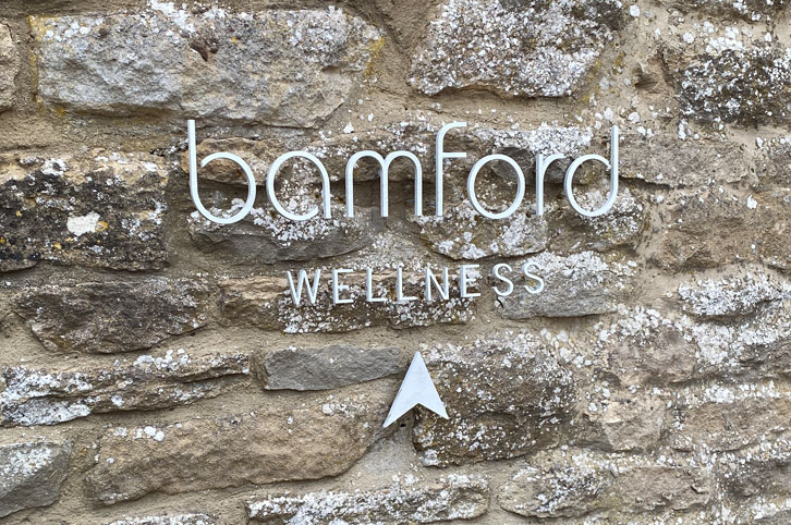 Laser cut white letters on a Cotswold stone wall at Bamfords Spa,