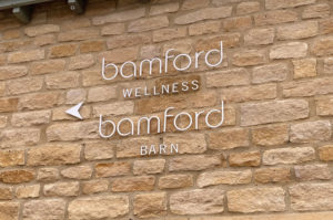 Laser cut white letters on a Cotswold stone wall at Bamfords Spa,