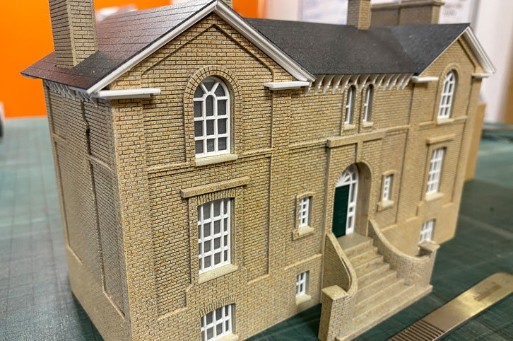 Close up of Harleston Station building model. Scalpel for scale on the table infront. The model is made of laser cut, etched and painted acrylic.